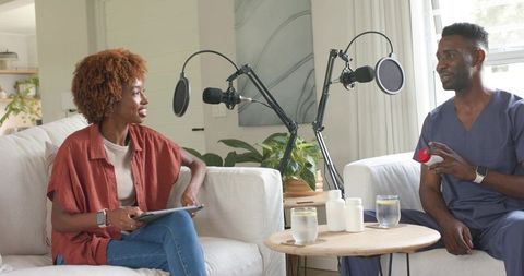 Podcast hosts discussing medication in cozy living room with microphones and pill bottles
