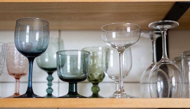 Assorted colored stemware displaying on wooden kitchen shelf with inverted wine glass