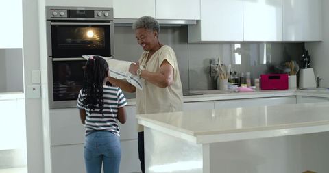Grandmother teaching granddaughter oven safety and baking in bright modern minimalist kitchen island