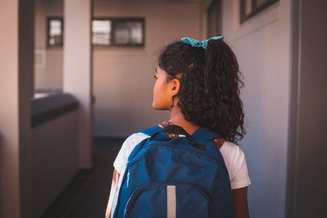 Rear view of biracial schoolgirl wearing backpack standing in school corridor. childhood and education at elementary school.