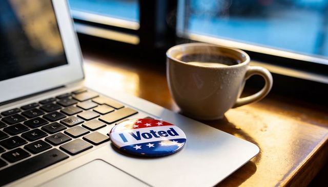 I voted button sitting on laptop trackpad with steaming coffee cup in morning workspace