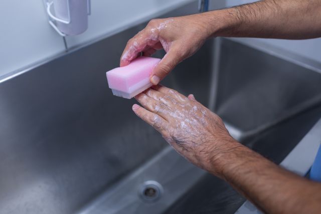 Close-up of a male surgeon scrubbing his hands with a brush at a hospital sink. This image can be used in healthcare and medical contexts to emphasize the importance of hand hygiene and sanitation before surgical procedures. Ideal for medical websites, educational materials, and hygiene awareness campaigns.