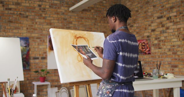 African american male painter painting from photograph on canvas in artist studio. art, creative and leisure time concept.