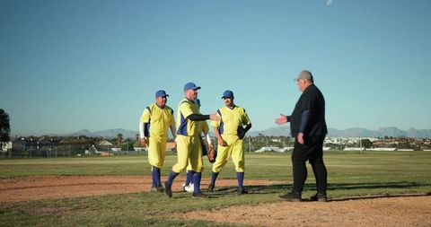 Baseball team greeting coach on pitcher's mound wearing yellow uniforms and blue caps