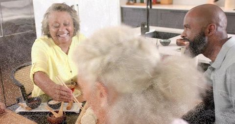 Smiling woman in yellow blouse serving food with chopsticks at family kitchen gathering
