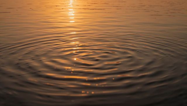 Golden dawn ripples on lake creating concentric circles with vertical sun reflection