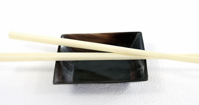 A pair of ivory chopsticks rests on a sleek black dish, with copy space. The simplicity of the arrangement suggests a minimalist approach to dining or Asian cuisine.