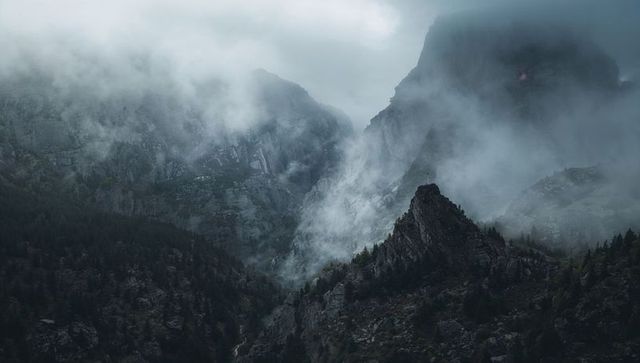 Jagged Rock Spire Rising Through Low Clouds Over Misty Alpine Valley, Moody Wilderness