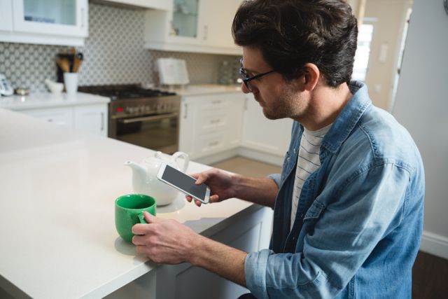 Man using mobile phone while having coffee in kitchen at home