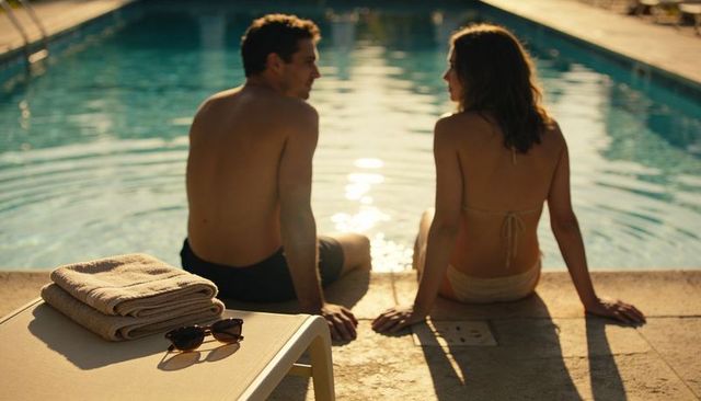 Couple relaxing and chatting at pool edge during golden hour with towels and sunglasses