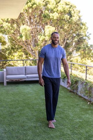 African american midlife man smiling while walking barefoot on terrace turf in casual tee