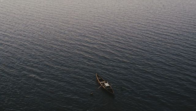 Solitary rower gliding across rippled dusk water in small wooden boat with covered seat