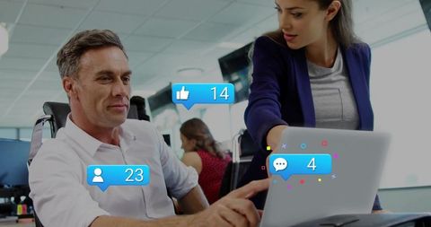 Collaborators pointing at laptop displaying social engagement icons in open-plan office