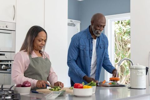 Mature black couple preparing meal in bright kitchen, chopping and rinsing vegetables