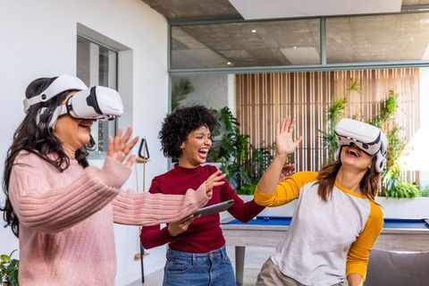 Multicultural women wearing VR headsets celebrating virtual game night in modern lounge