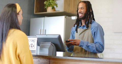 Smiling barista processing contactless smartphone payment at wooden cafe counter with qr code