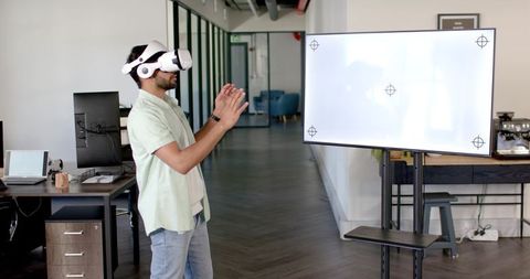 Indian man wearing vr headset interacting with virtual interface in modern open office