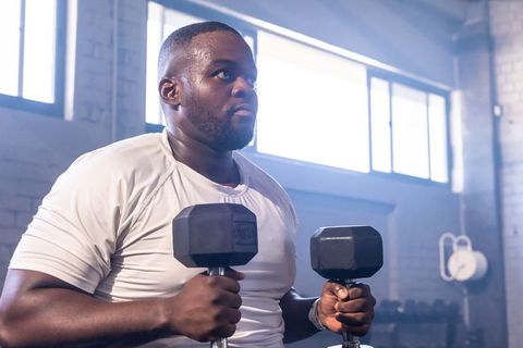 African man lifting heavy hex dumbbells in industrial gym, focused strength training
