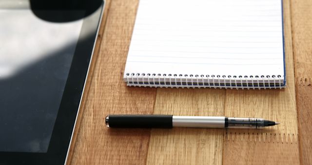 A blank notepad lies next to a pen and a tablet on a wooden surface, with copy space. The setup suggests a professional or educational environment, ready for note-taking or brainstorming.
