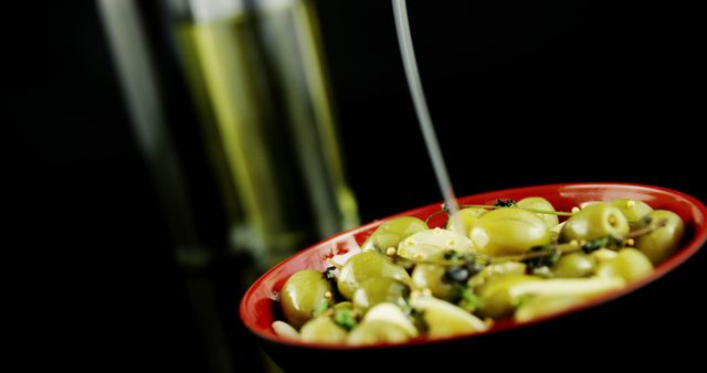 Pouring Olive Oil Over Green Olives in Red Bowl on Black Background - Download Free Stock Images Pikwizard.com