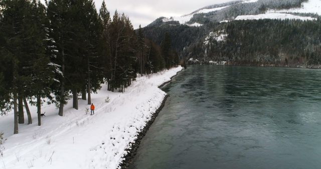 Lone Traveler Walking along Snow-covered Path beside Tranquil River in Winter Landscape - Download Free Stock Images Pikwizard.com