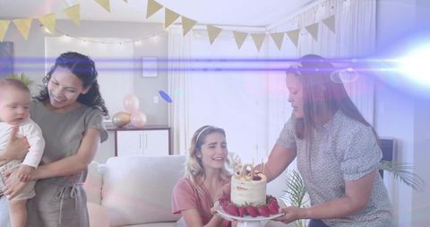 Presenting birthday cake with candles and strawberries to smiling woman on sofa