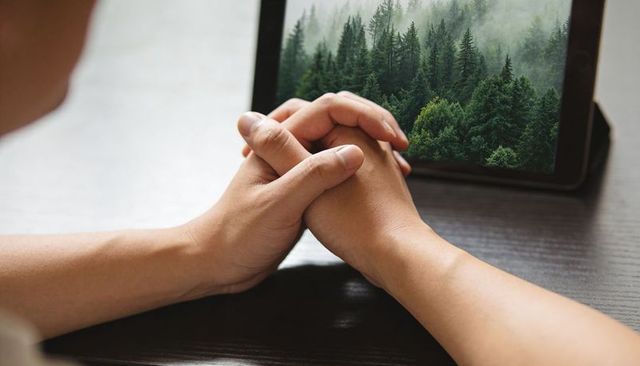 Clasped hands over tablet showing misty forest, symbolizing digital connection to nature