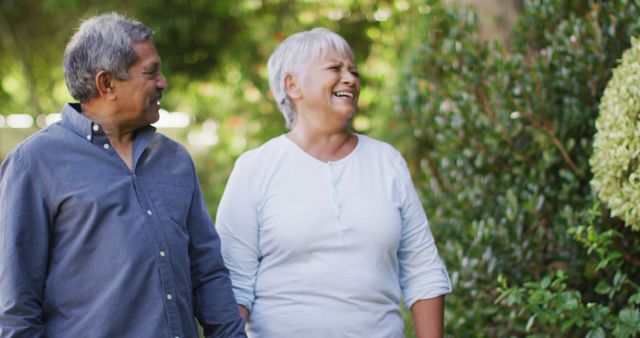 Image of happy biracial senior couple holding hands and walking in garden. active retirement lifestyle, senior relationship and spending time together concept.