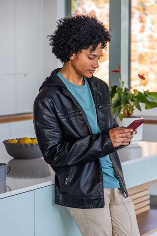 African american man leaning on counter texting on red phone in leather jacket