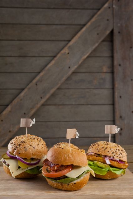 Assorted gourmet hamburgers with fresh ingredients such as cheese, lettuce, tomato, and onion, displayed on a wooden table with food tags. Ideal for use in food blogs, restaurant menus, culinary websites, and promotional materials for food-related events.
