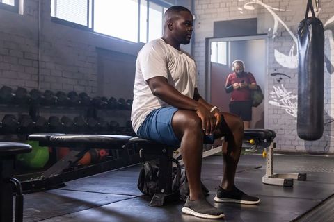 African american man resting on gym bench after workout near dumbbells and punching bag