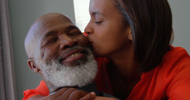 Elderly man with grey beard receiving loving kiss from his daughter. Gentle moment highlighting familial affection and emotional bond. Ideal for advertising family values, elderly care, or health insurance products.