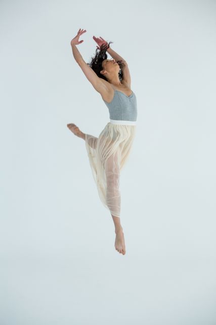 This image captures a contemporary dancer mid-leap in a studio, showcasing grace and athleticism. Ideal for use in articles, blogs, or promotional materials related to dance, fitness, performing arts, and creative expression. Perfect for illustrating concepts of movement, elegance, and dedication in dance.