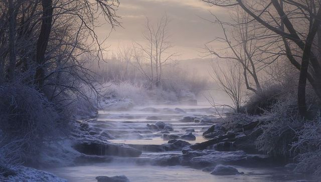 Misty winter stream flowing over frosted rock cascades at soft sunrise light