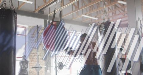 Shirtless boxer punching red speed bag with hand wraps and blue shorts in sunlit brick gym