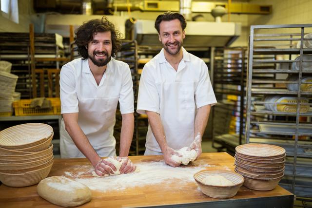 Two smiling bakers kneading dough on the counter