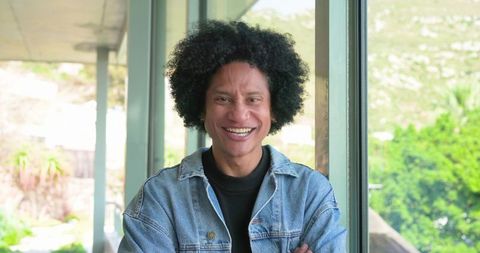 Smiling african american man in denim jacket standing by sunroom window, midlife portrait