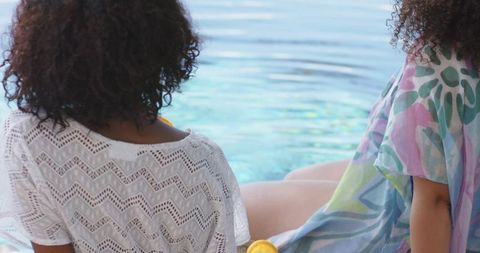 Two african american women relaxing poolside in crochet cover-up and colorful kaftan