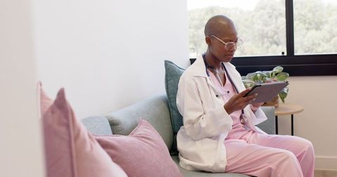 Female doctor reviewing tablet on clinic sofa in pastel lounge, casual telemedicine