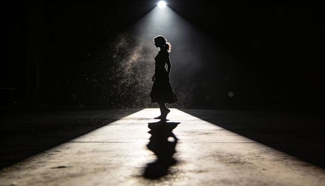 Silhouette woman standing in spotlight on empty stage casting long shadow and dust motes