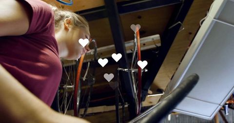 Woman exercising on stationary bike trainer in garage with heart icons