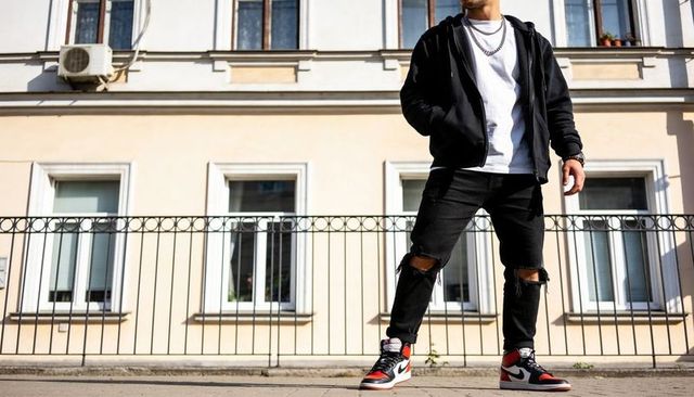 Urban streetwear model posing in black hoodie, ripped jeans and high-top sneakers