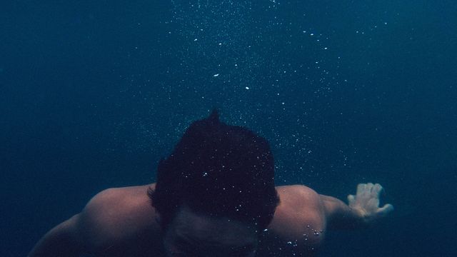 Man swimming underwater in deep ocean with air bubbles visible around him. Perfect for use in environmental campaigns, sports and adventure promotions, fitness and health projects, travel brochures, or underwater exploration advertisements.