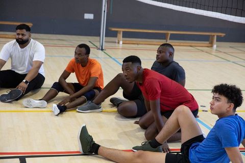 Multicultural male volleyball team stretching on gym floor before training