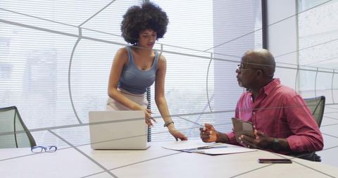 Professionals collaborating over tablet and laptop in modern glass boardroom discussion