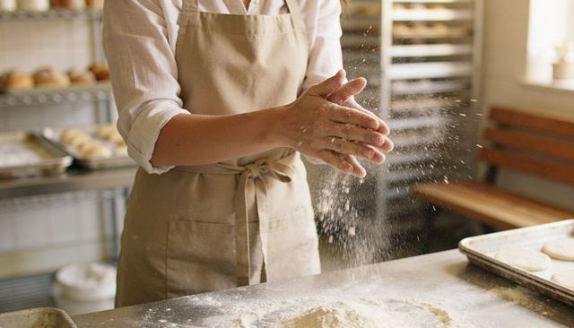 Baker dusting work surface with flour, clapping hands, preparing dough in artisan bakery