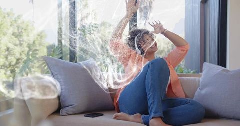 Woman pressing hands on soapy window relaxing on sofa with headphones and smartphone nearby
