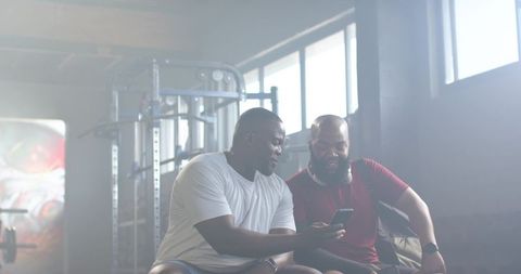 African american men checking phone after workout in gym, wearing headphones and smartwatch