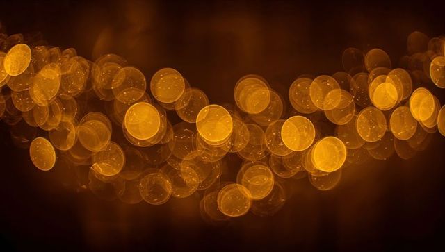 Glowing amber bokeh orbs drifting across dark backdrop with speckled reflections and shimmer
