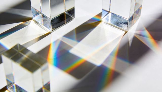Crystal prism blocks casting rainbow spectra and geometric shadows on white surface